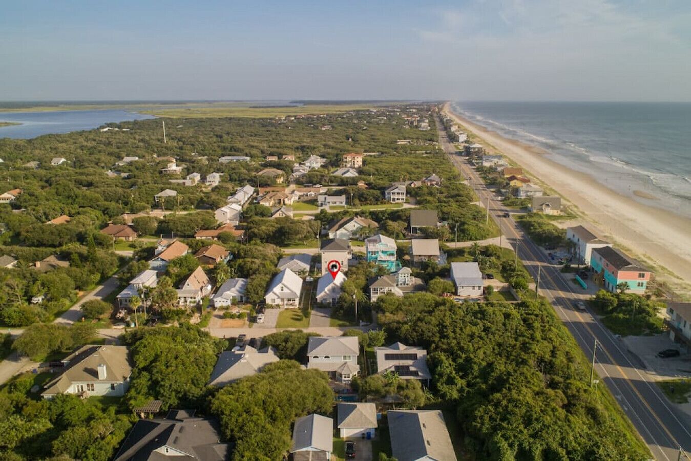 An aerial view of a coastal residential area with houses, a beach, and a road.