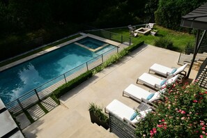Ein rechteckiger Pool mit einer umlaufenden Sonnenterrasse, Liegestühlen und einer Feuerstelle.