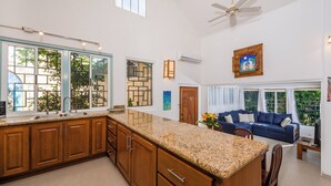 A spacious kitchen with granite countertops, wooden cabinets, and a large island. There is a dining area with a blue sofa and a television.