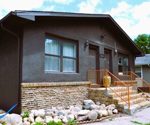 A two-story building with a stone foundation, a metal staircase with orange railings, and a door marked "1322".