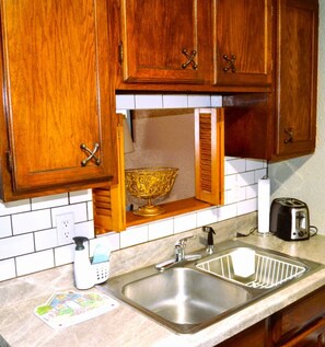 Una cocina con armarios de madera, un lavamanos de acero inoxidable, un tostador y un cuenco decorativo.