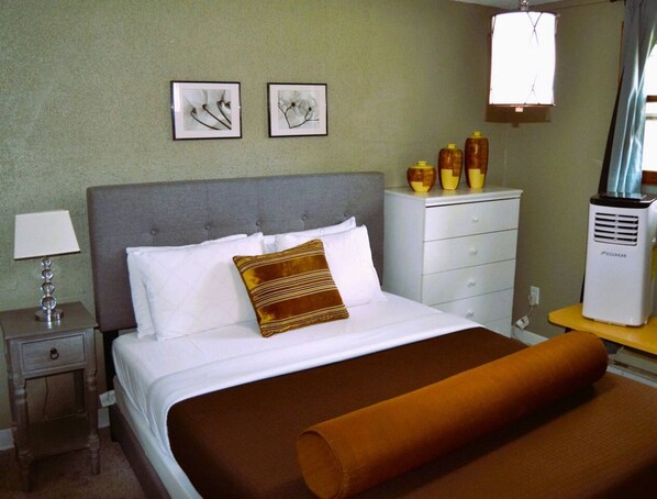 A hotel room with a bed, a nightstand with a lamp, a dresser, and two framed artworks on the wall.