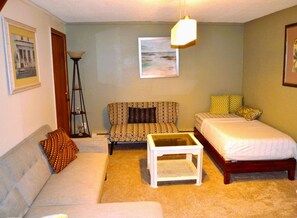 A small, cozy room with a sofa, a chair, a bed, and a small table.