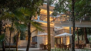 Un espacio al aire libre con varios niveles, mesas y sillas para comer, rodeado de árboles y un edificio de diseño moderno.