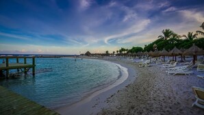 Una playa con un muelle de madera, sillas de descanso y sombrillas de paja.