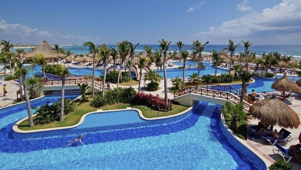 Un resort con varias piscinas, palmeras y una zona de playa.