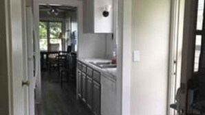 A narrow hallway leading to a kitchen with white cabinets and a dining area.