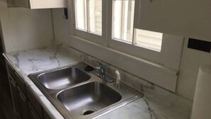 A kitchen with two stainless steel sinks, a marble countertop, and a window with blinds.