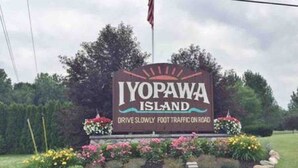 A sign for IYOPAWA ISLAND with a message to drive slowly and foot traffic on the road.