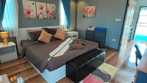 A modern bedroom with a large bed, a bedside table, a bench, and a wall-mounted air conditioner. - Cozy house 1 BR, close to the beach (Tambon Choeng Thale)
