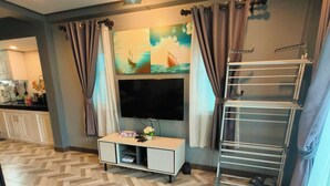 A modern living room with a flat-screen TV, a white entertainment unit, a wooden dining table, and a patterned rug. - Cozy house 1 BR, close to the beach (Tambon Choeng Thale)