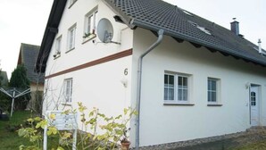 Een tweelaags huis met een witte buitenkant, een grijs dak en het nummer '6' aan de zijkant.