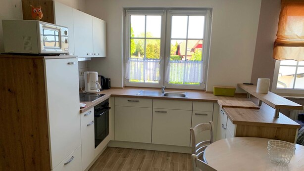 Een kleine keuken met witte kastjes, een magnetron, een koffiezetapparaat en een raam met uitzicht op groen.
