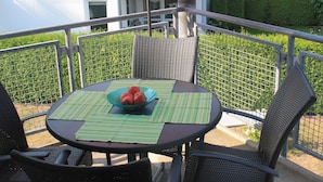 An outdoor patio with a table and chairs, a red umbrella, and a view of a building with a green roof. - Apartment on the beach - apartment (Karlshagen)