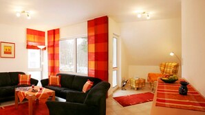 A living room with a black sofa, a wooden coffee table, and a red and orange striped curtain. - Apartment on the beach - apartment (Karlshagen)