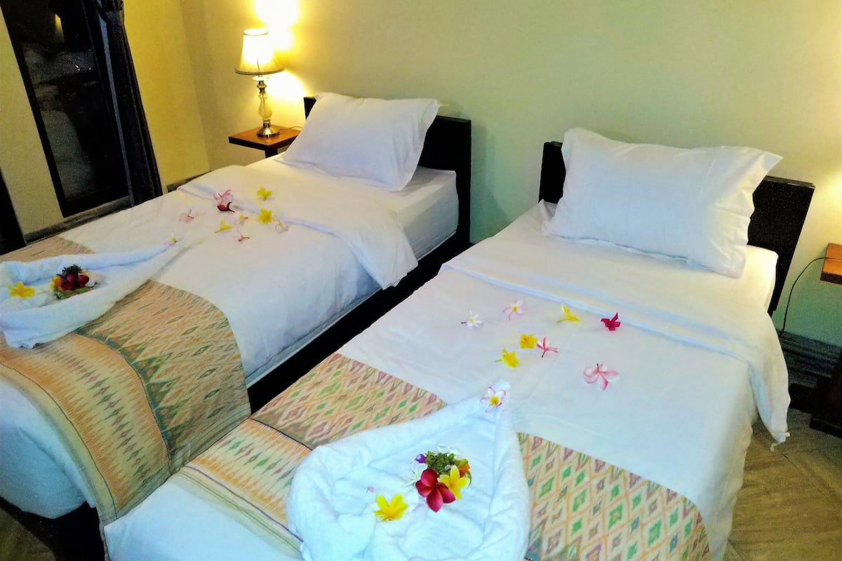 Two single beds with white linens, each with a floral arrangement and a towel.