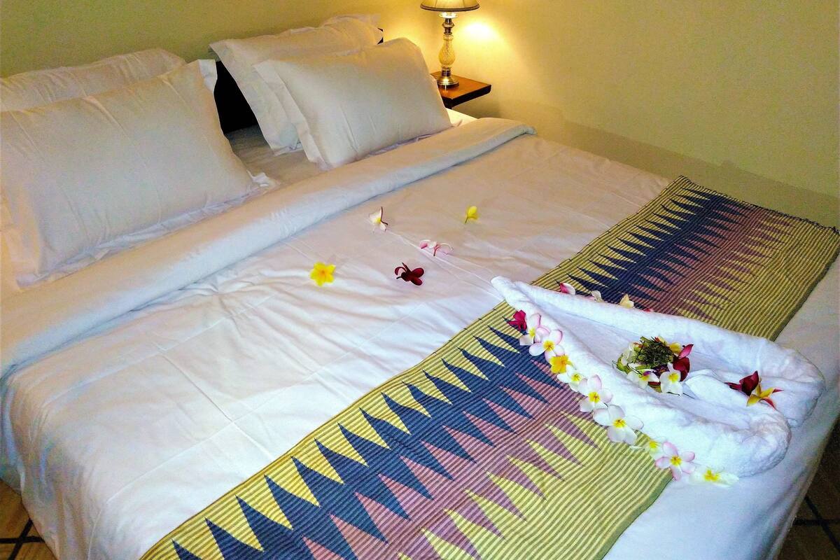 A neatly made bed with white linens, a patterned blanket, and a small table with a lamp beside it.