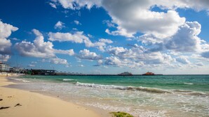 Una platja amb un moll que s'endinsa a l'aigua, un edifici a l'esquerra i un vaixell a la distància.