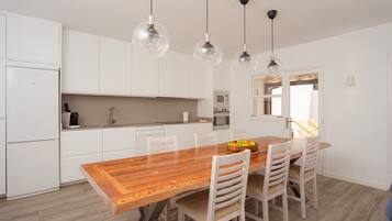 A modern kitchen with white cabinets, a wooden dining table, and three pendant lights.