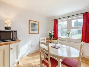Een keuken met een magnetron, een eettafel met stoelen, een raam met rode gordijnen en een lijst met een foto aan de muur.