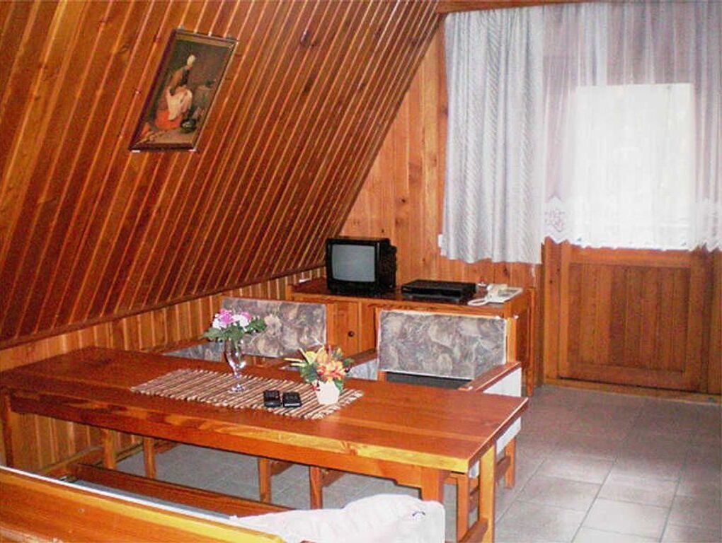 A wooden interior with a dining table, chairs, a television, and a window with curtains.
