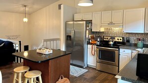 A modern kitchen with white cabinets, stainless steel appliances, and a central island with stools. -  Great 5 Bedroom in Beautiful Bonnet Shores, Narragansett R (Narragansett)