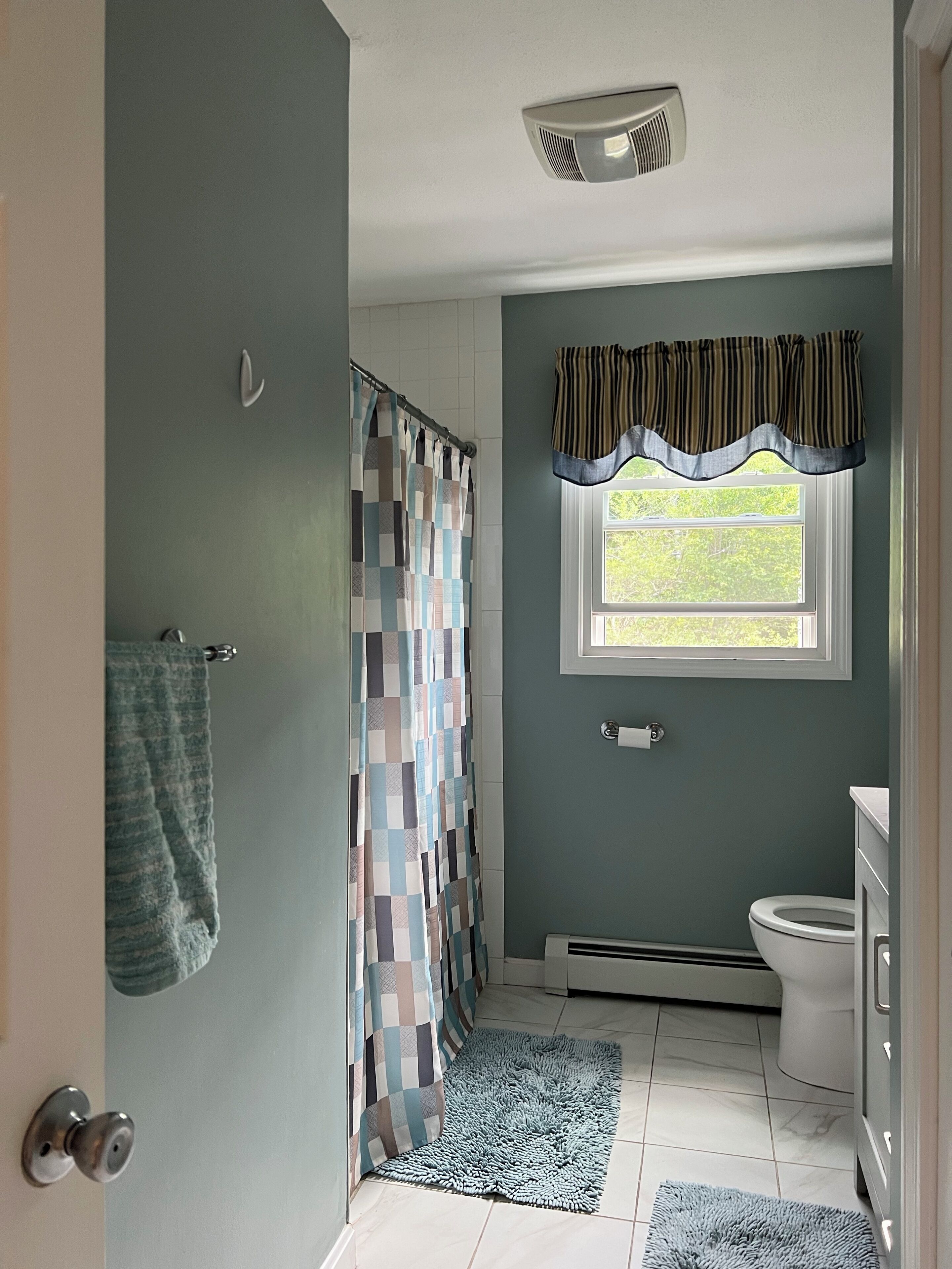 A bathroom with a shower curtain, a window with a valance, a toilet, and a towel rack.