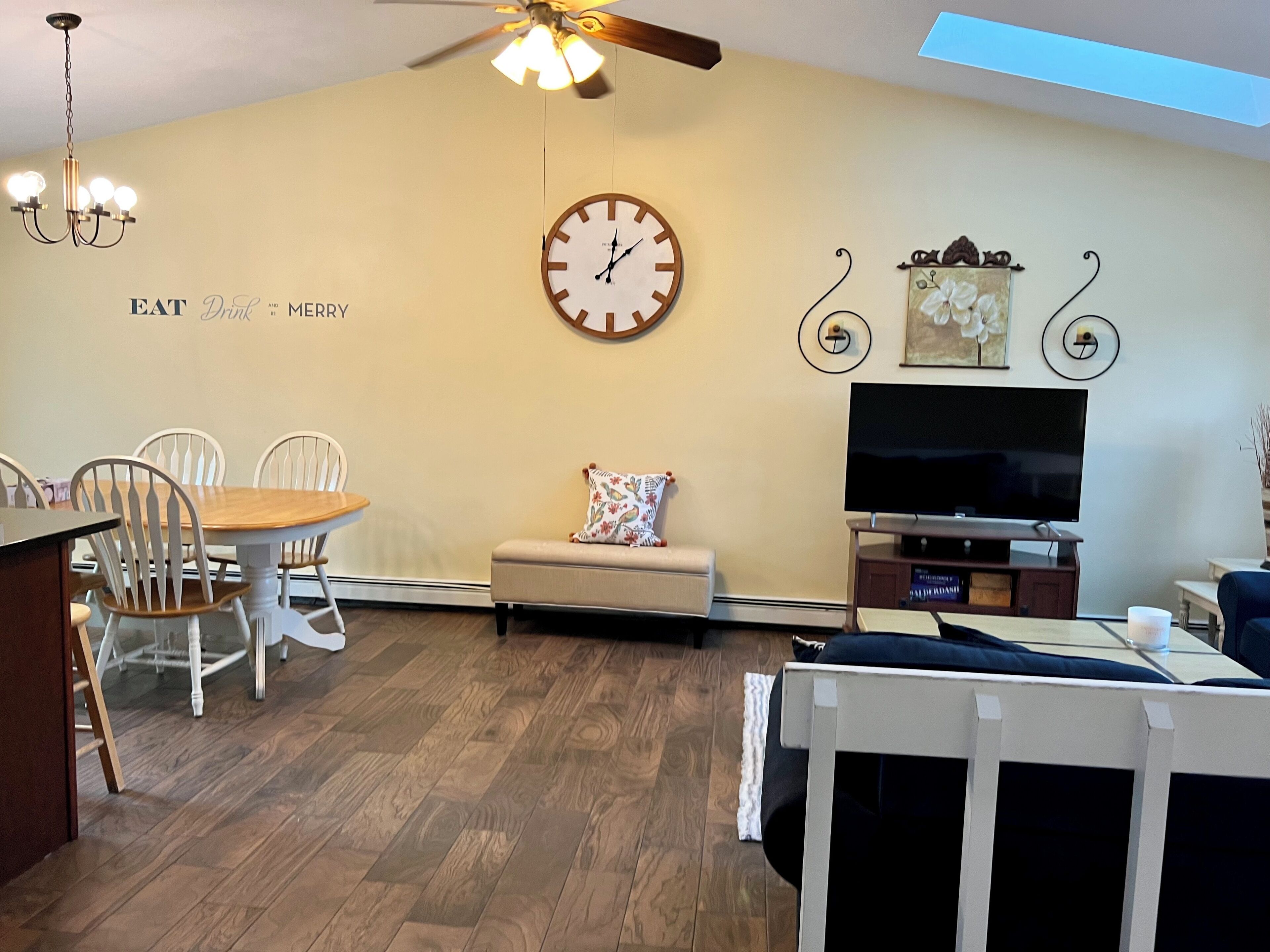 A living room with a dining area, a clock, a TV, and a ceiling fan.