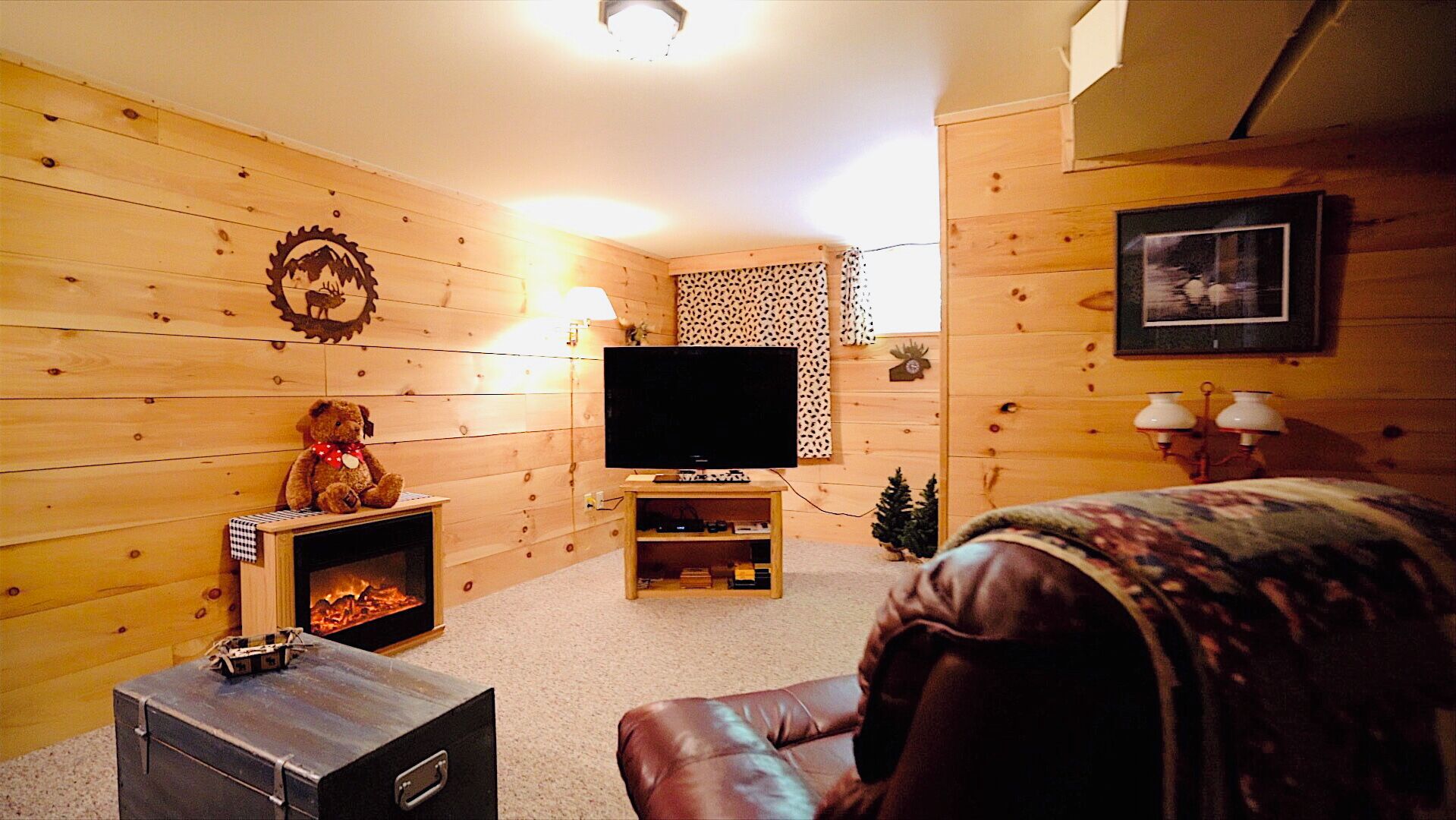 A cozy living room with wooden walls, a fireplace, a television, and a leather sofa.