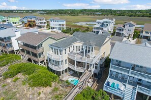A coastal residential area with multi-story houses featuring balconies, a small pool, and a view of the beach.