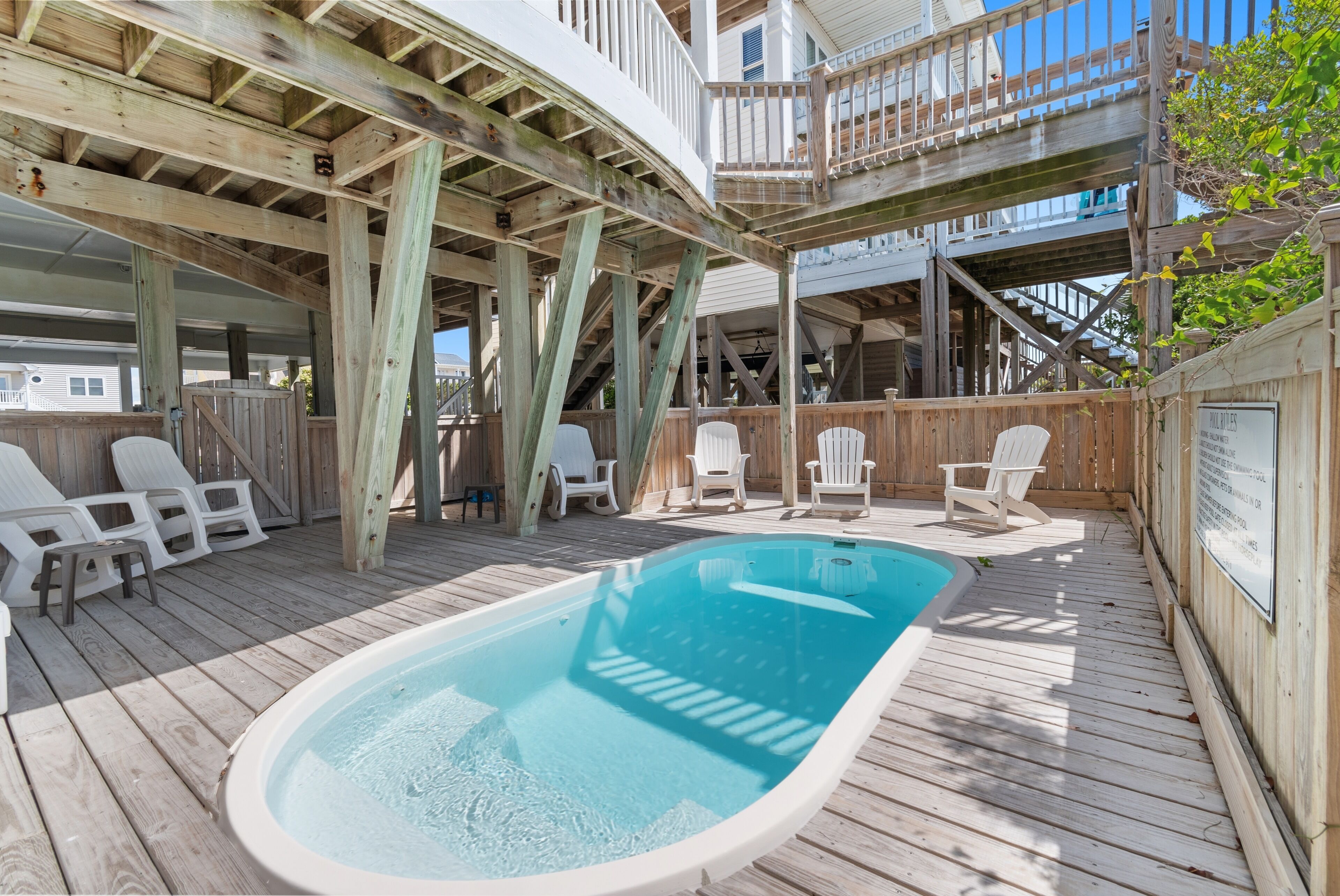 A wooden deck with a hot tub, white chairs, and a wooden staircase.