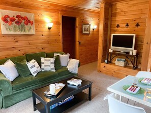 A cozy room with a green sofa, a coffee table, a TV, and a painting of red flowers. - Luxurious & secluded mansion and separate cabin with stunning ocean views! (Winter Harbor)