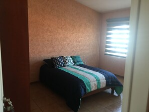 Un dormitorio con cama, almohadas y una ventana con persianas.