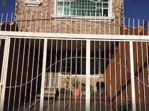 Una entrada protegida con un portón de metal y un muro de piedra.