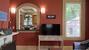 Una sala de estar con chimenea, televisor y un cartel que dice 'NOCHE DE CINE'.