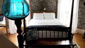 Una cama con dosel con sábanas blancas, papel tapiz floral y suelo de madera.