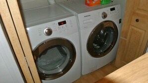 A Samsung front-loading washer and dryer in a laundry room with a wooden door and a white tiled wall. - The Mont-Royal - appattement apartment (montreal)