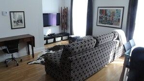 A living room with a patterned sofa, a flat-screen TV, a desk with a chair, and artwork on the walls. - The Mont-Royal - appattement apartment (montreal)
