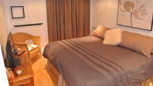 A bedroom with a bed, a television, a chair, and a curtain. - The Mont-Royal - appattement apartment (montreal)