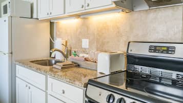 A kitchen with white cabinets, a granite countertop, a microwave, a toaster, and a stove.