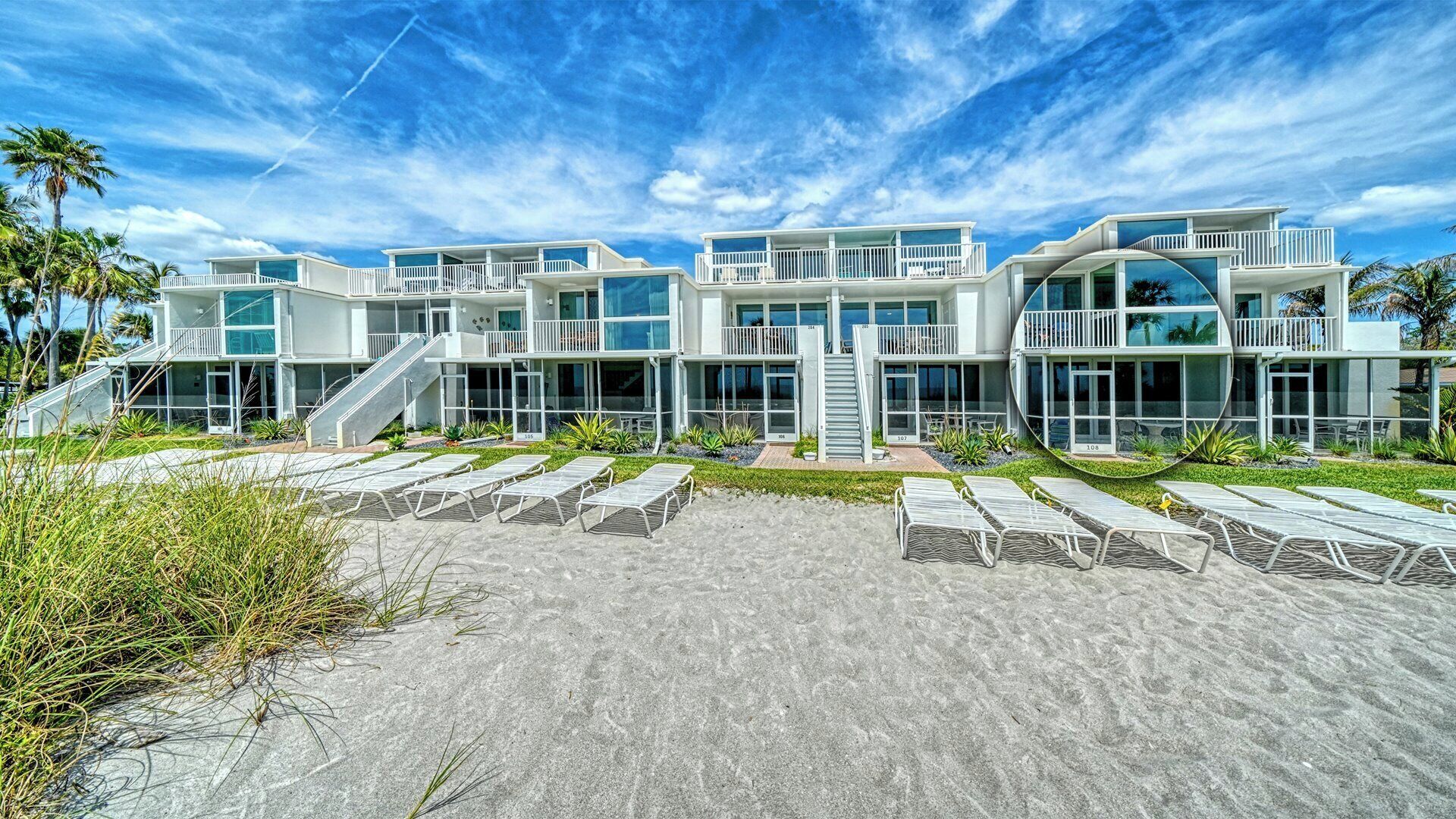 Een modern pand aan het strand met meerdere verdiepingen, buiten zitplaatsen en een trap naar de ingang.