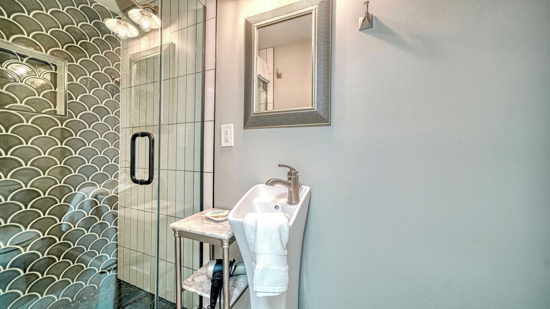 A bathroom with a tiled wall, a sink, a mirror, and a towel rack.