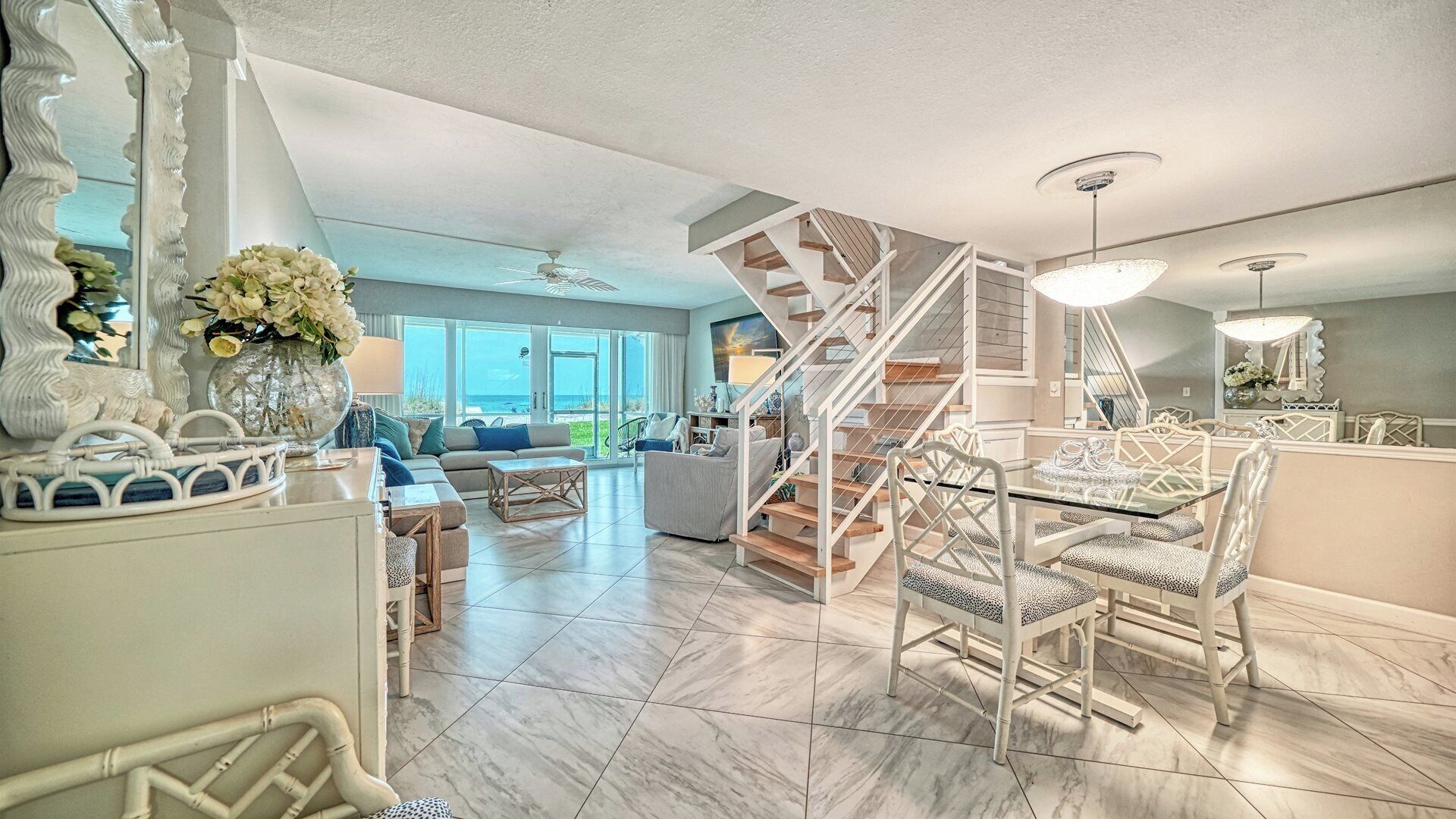 A spacious living area with a modern staircase, a dining table with chairs, and a view of the outdoors.
