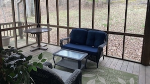 A covered outdoor seating area with a wicker sofa, a small table, and a chair.