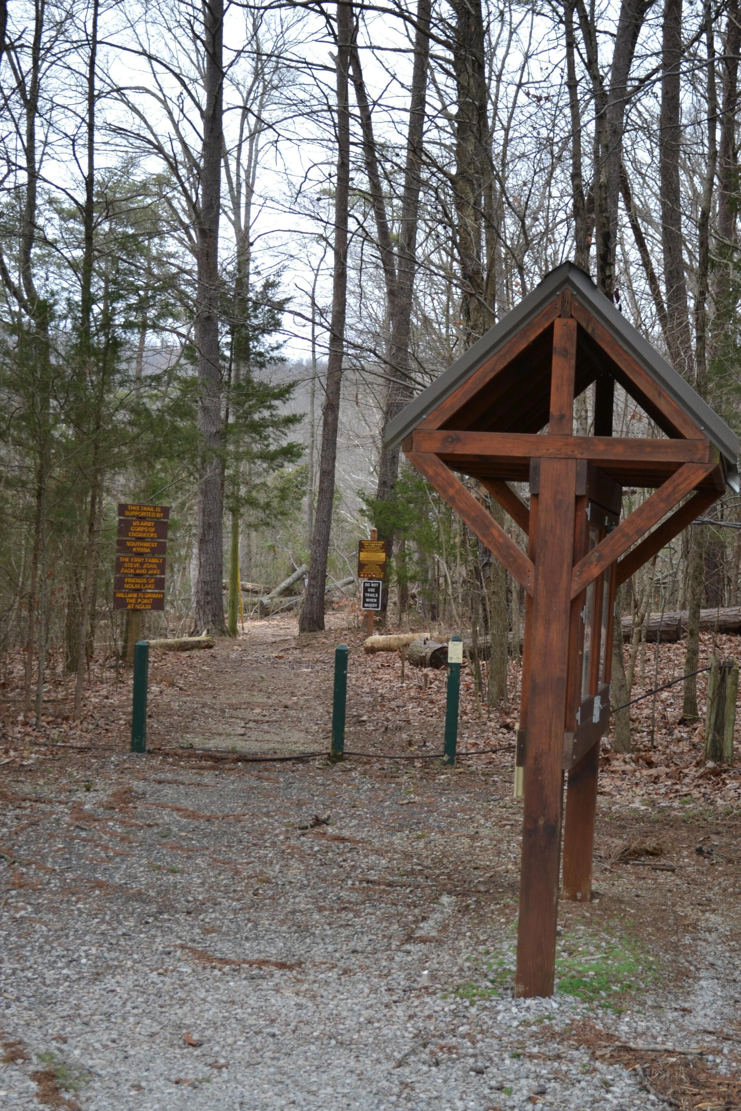 Un panneau indicateur en bois, placé dans une zone boisée, qui fournit des informations sur les directions à suivre.