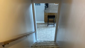 A wooden staircase with a handrail, leading to a room with a kitchen area visible through an open door.