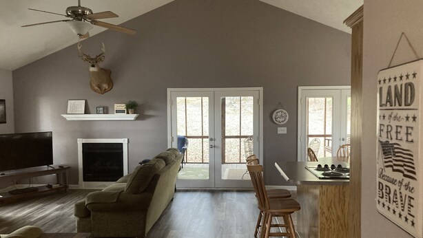 A spacious living room with a fireplace, a television, a sofa, and a ceiling fan.