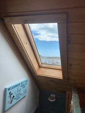 A skylight in a room with a view of boats on water, a wooden ceiling, and a wall with a motivational quote. - A Quaint Rustic Bungalow Overlooking The Fishing Village of Corea Harbor (Gouldsboro)