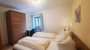 Un dormitorio con cama, armario de madera, escritorio y ventana con cortinas.
