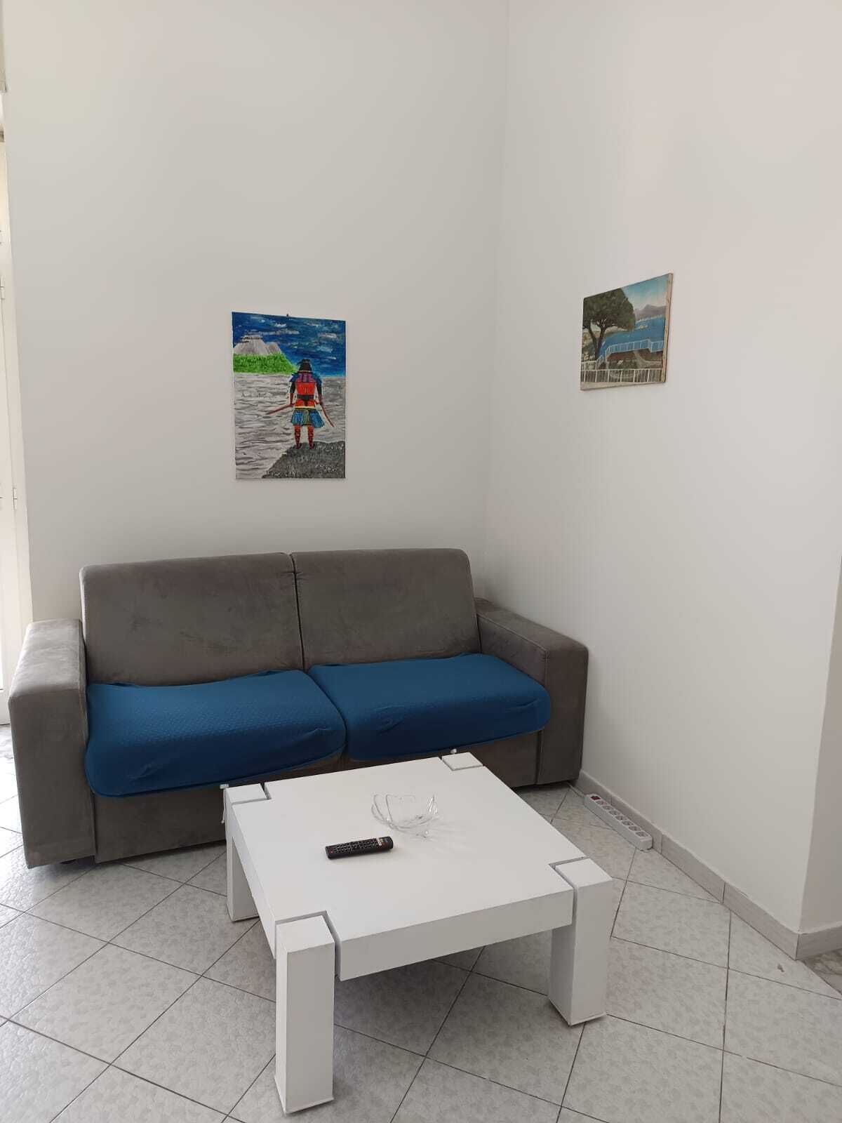 Una sala de estar con un sofá gris y cojines azules, una mesa de centro blanca y dos cuadros en las paredes.